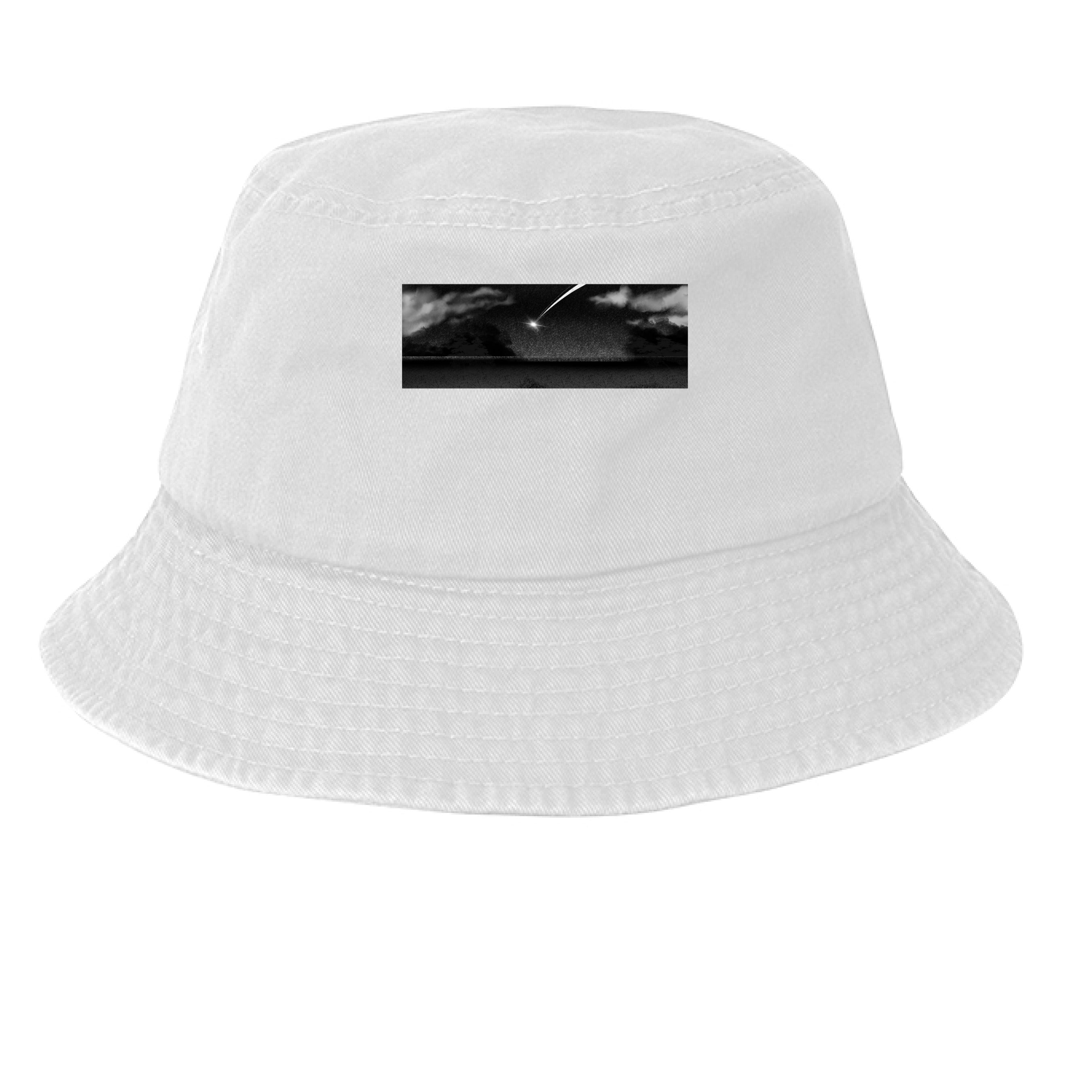 This is the White Star Fall Bucket Hat by Lee Hansheng Studios. This is showcasing the hat from the front. The illustration is a meteor streaking through the sky. It is a moody piece that as gradients of black and grey, a little pixelated with white clouds in the forefront. The meteor is also white. It is a smaller rectangular than the cap. It is against a white background.