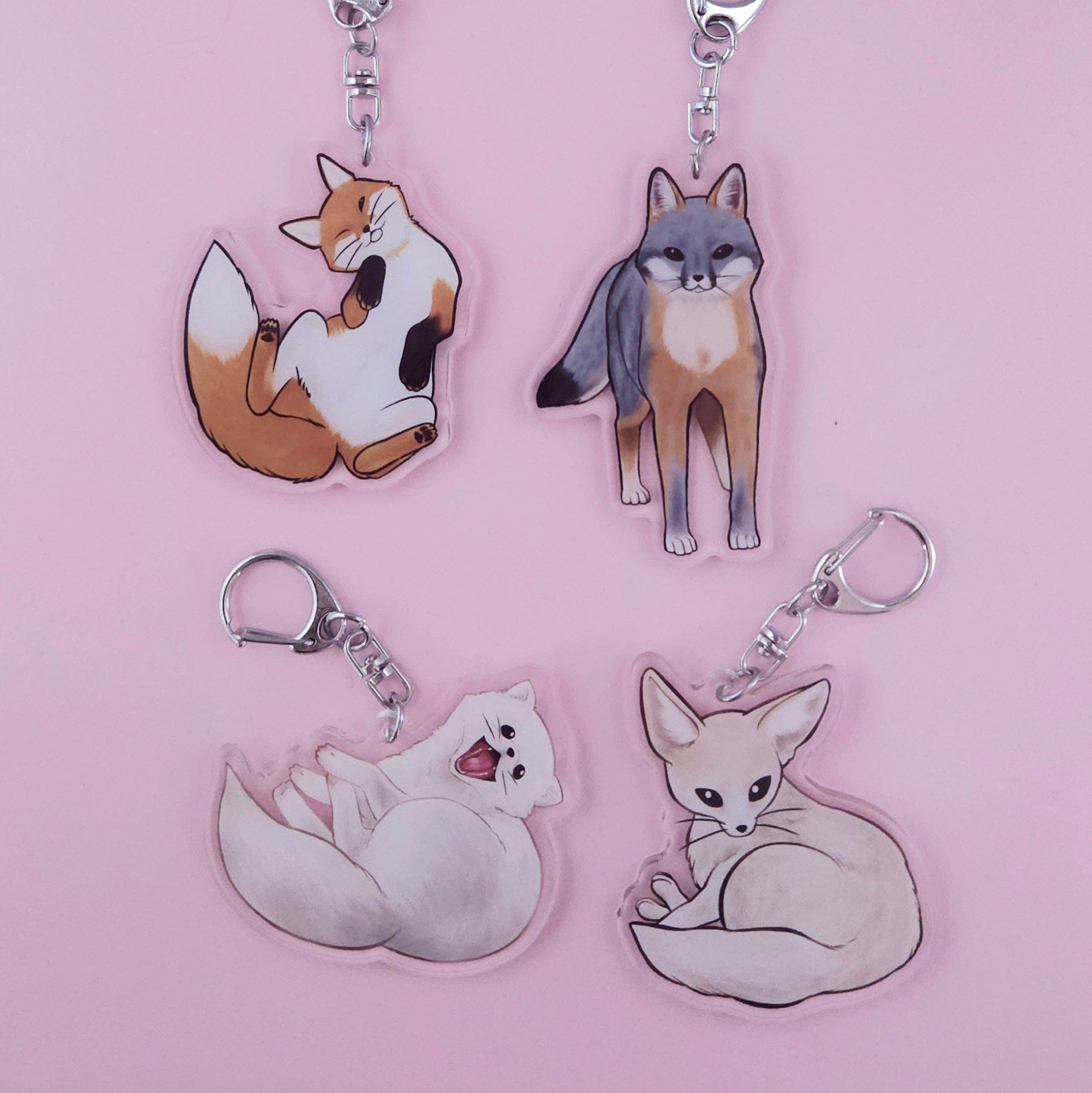 Four fox-themed keychains on a pink background