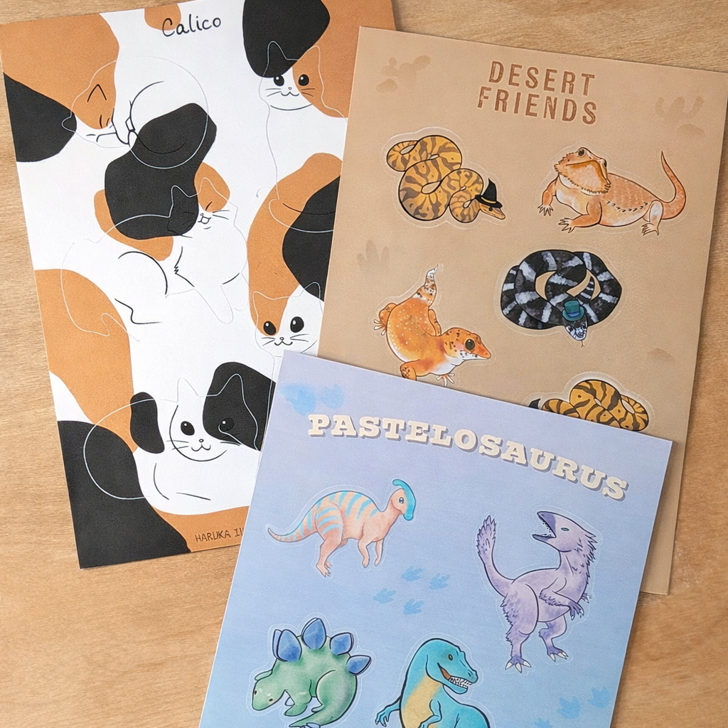 Three sticker sheets with animal illustrations on a wooden surface